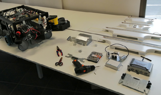 D) The battery is enclosed in a steel box and held by a retaining plate to prevent movement and connected to a DP9 connector and DC 24V wires.